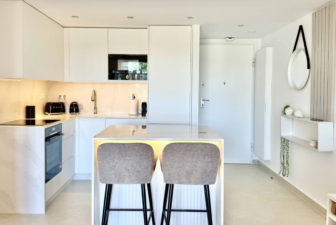 Modern white kitchen with breakfast island in an upgraded one-bedroom apartment for sale on Mar Menor Golf Resort by Levante Properties.