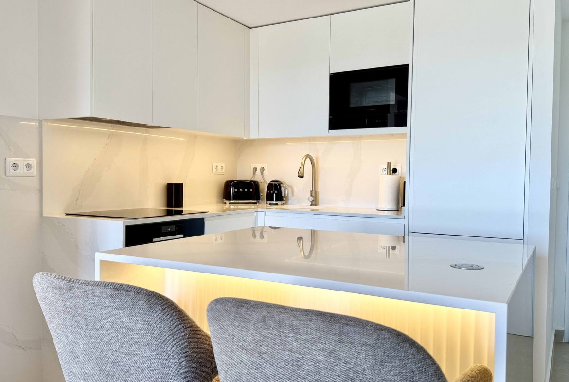 Modern white kitchen with breakfast island in an upgraded one-bedroom apartment for sale on Mar Menor Golf Resort by Levante Properties.
